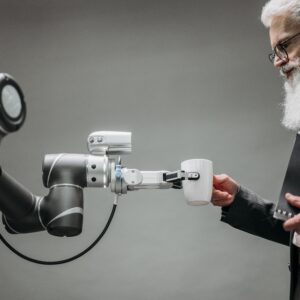 An elderly man receives a cup from a robotic arm in a modern office setting.